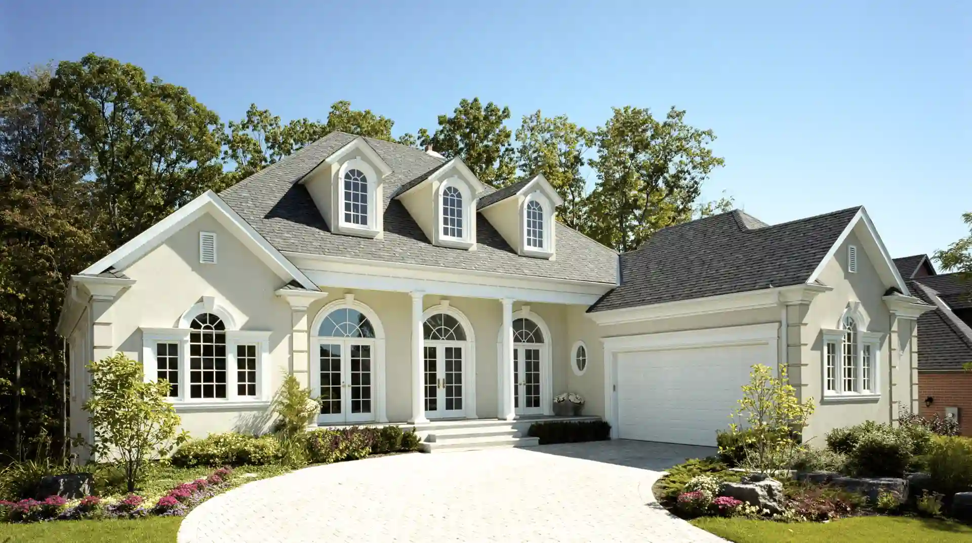Casa elegante de estilo clásico con fachada blanca, ventanas arqueadas y jardín bien cuidado.