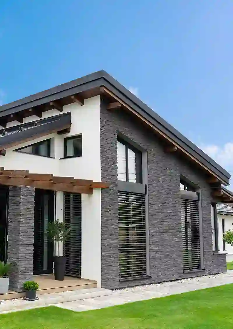 Casa moderna con fachada de piedra gris, techo inclinado y amplio jardín.